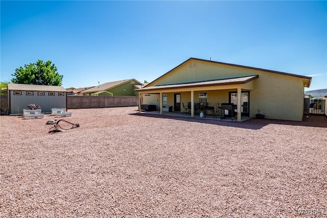 rear view of property featuring a fenced backyard, stucco siding, a storage unit, an outbuilding, and a patio