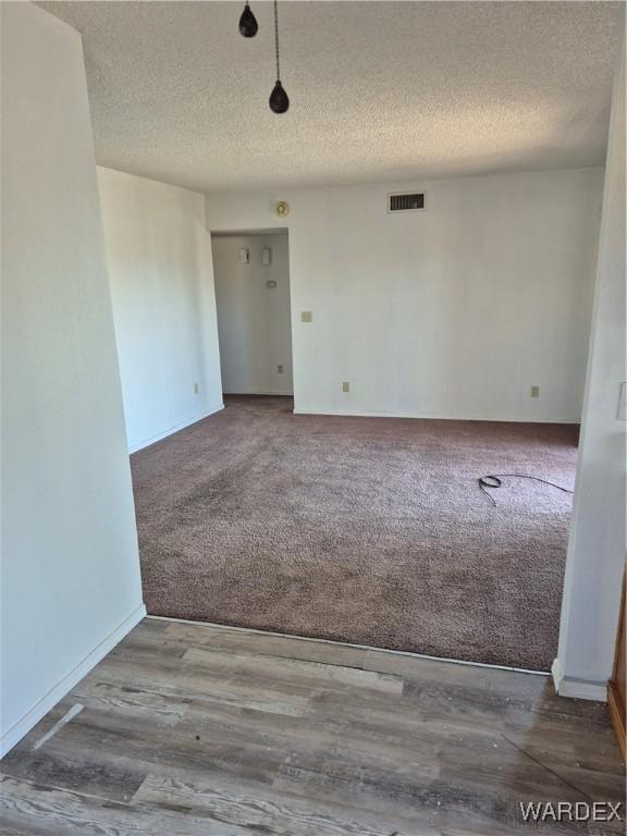 spare room featuring a textured ceiling, visible vents, carpet flooring, and baseboards