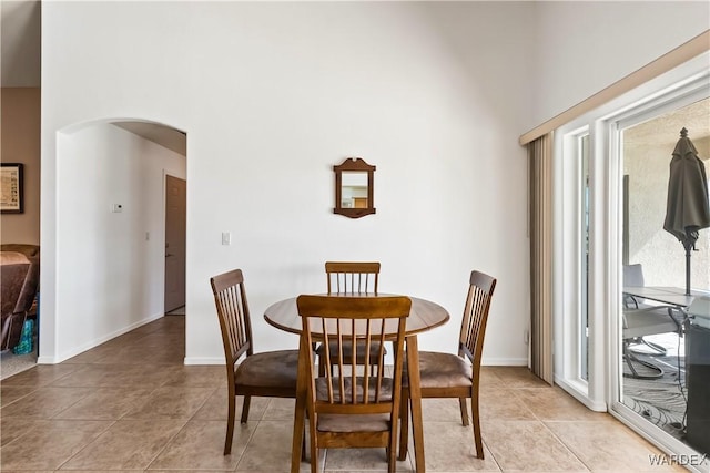 dining area featuring arched walkways, a towering ceiling, baseboards, and light tile patterned floors