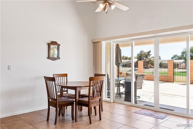 dining area with a ceiling fan, light tile patterned flooring, a towering ceiling, and baseboards