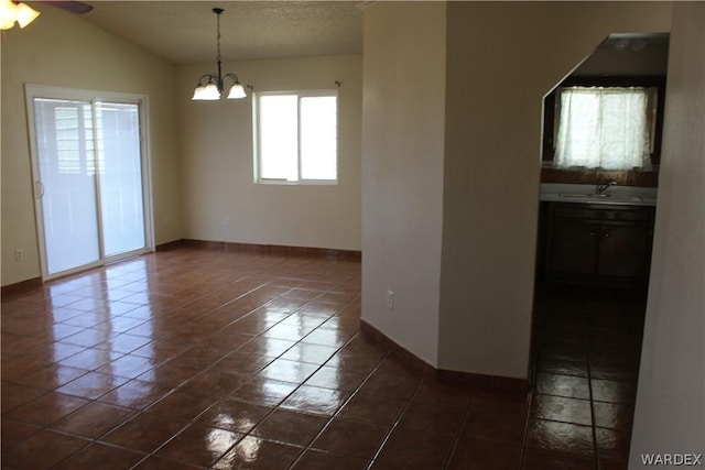 empty room featuring a textured ceiling, lofted ceiling, dark tile patterned flooring, a sink, and baseboards