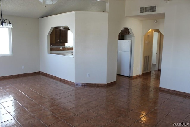 unfurnished room featuring arched walkways, a textured ceiling, dark tile patterned floors, visible vents, and baseboards