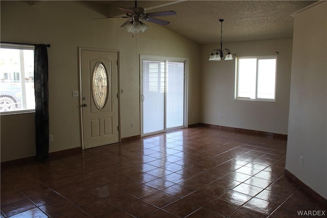 foyer entrance with lofted ceiling, a textured ceiling, dark tile patterned flooring, baseboards, and ceiling fan with notable chandelier