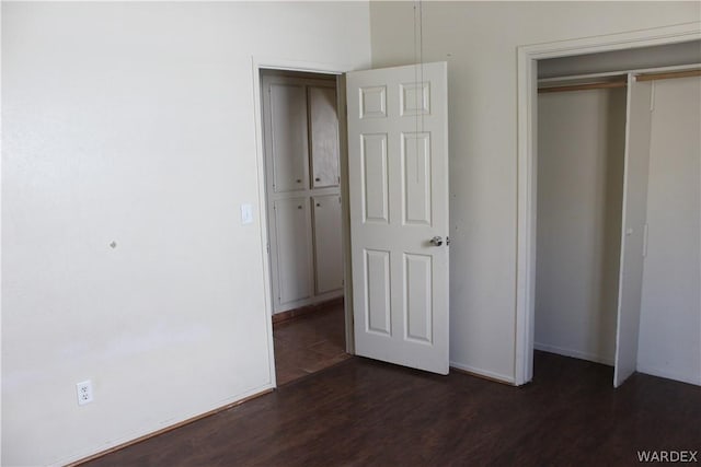 unfurnished bedroom with a closet, baseboards, and dark wood-type flooring