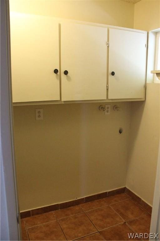 laundry area featuring cabinet space, dark tile patterned floors, and baseboards