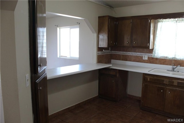 kitchen with dark brown cabinets, dark tile patterned floors, a sink, and light countertops