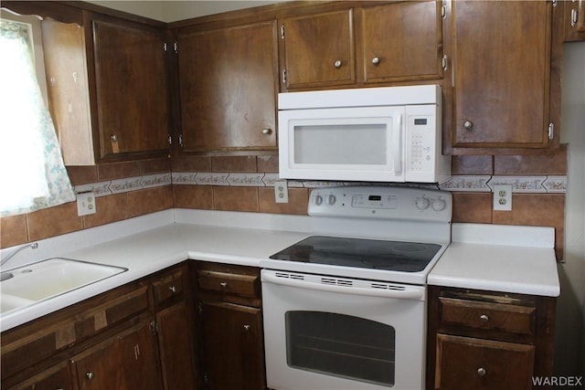 kitchen with light countertops, white appliances, backsplash, and a sink