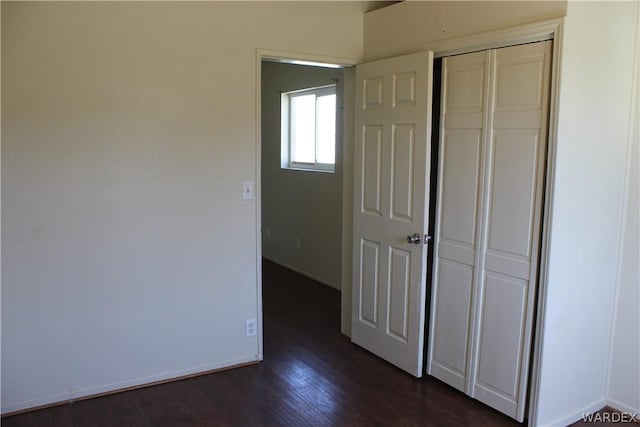 unfurnished bedroom featuring dark wood-style floors, a closet, and baseboards