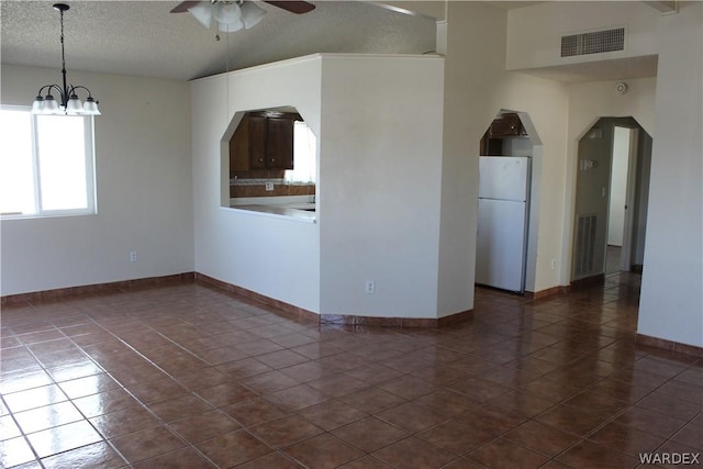 empty room featuring a textured ceiling, arched walkways, ceiling fan with notable chandelier, dark tile patterned floors, and visible vents