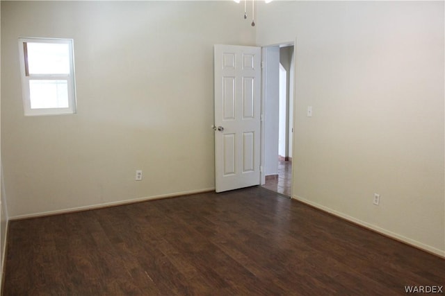 spare room with baseboards and dark wood finished floors