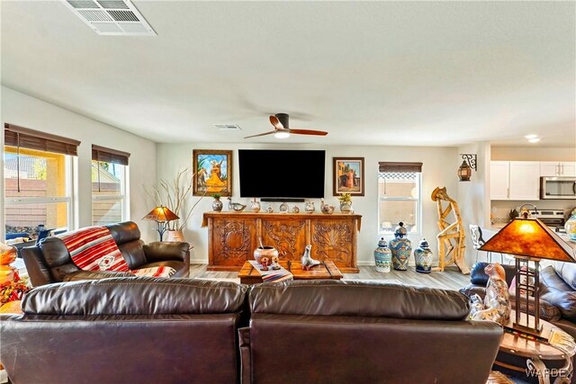 living area with a ceiling fan, visible vents, baseboards, and wood finished floors