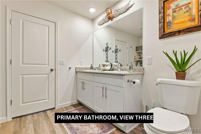 bathroom featuring double vanity, toilet, a sink, and wood finished floors