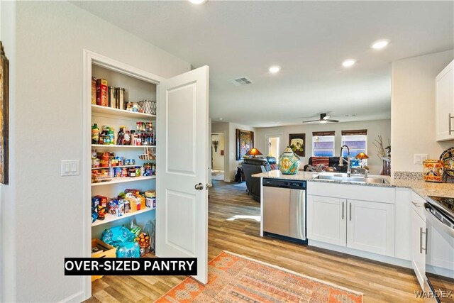 kitchen with a sink, visible vents, white cabinets, open floor plan, and stainless steel dishwasher