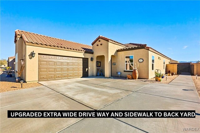 mediterranean / spanish-style house featuring stucco siding, a gate, a garage, driveway, and a tiled roof