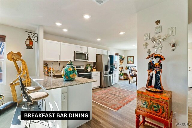 kitchen with a peninsula, a sink, white cabinets, appliances with stainless steel finishes, and dark stone countertops