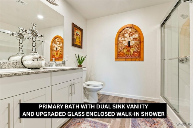 bathroom with double vanity, visible vents, a stall shower, a sink, and wood finished floors