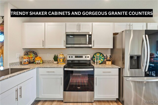 kitchen featuring stainless steel appliances, a sink, white cabinetry, and light stone countertops