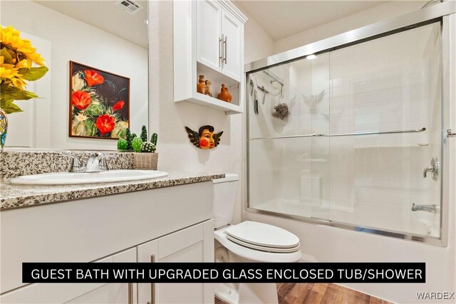 bathroom featuring toilet, shower / bath combination with glass door, visible vents, and vanity