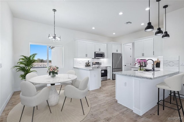 kitchen with appliances with stainless steel finishes, white cabinetry, a peninsula, and decorative light fixtures