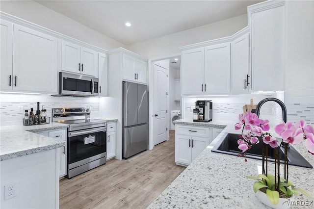 kitchen featuring stainless steel appliances, decorative backsplash, white cabinetry, and light wood-style floors