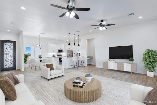 living room featuring ceiling fan with notable chandelier, light wood-type flooring, visible vents, and recessed lighting