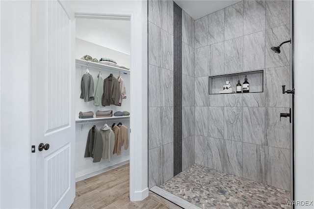 bathroom with a spacious closet, tiled shower, and wood finished floors