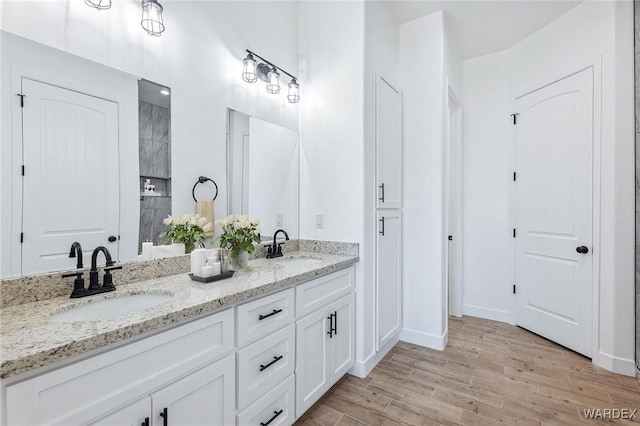 full bathroom featuring double vanity, a sink, baseboards, and wood finished floors