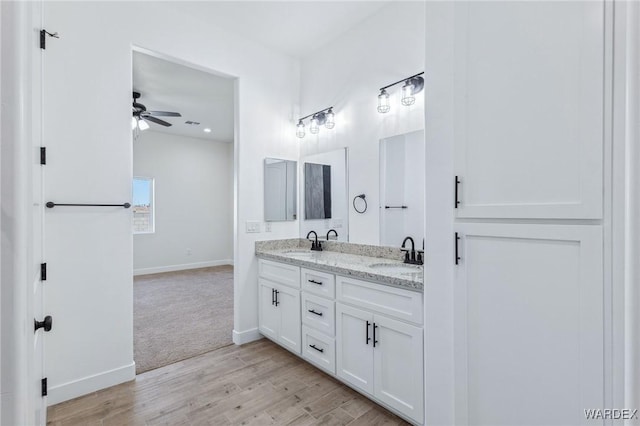 full bathroom with double vanity, baseboards, a sink, and wood finished floors