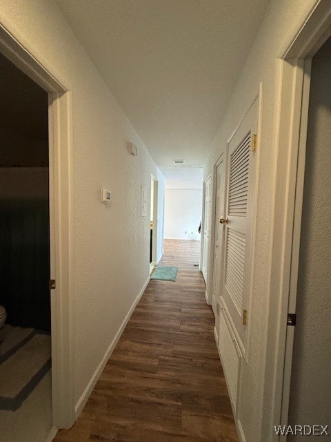 hall with a textured wall, dark wood-type flooring, and baseboards