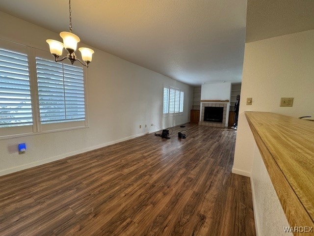 unfurnished living room featuring a notable chandelier, a fireplace, baseboards, and dark wood-style flooring