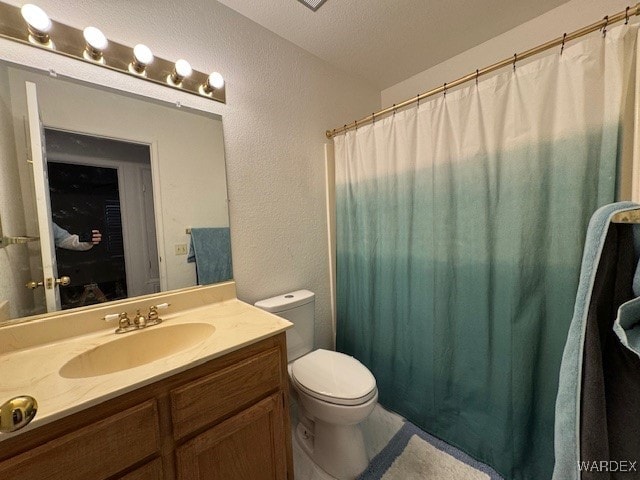 full bath featuring toilet, a textured wall, a textured ceiling, and vanity