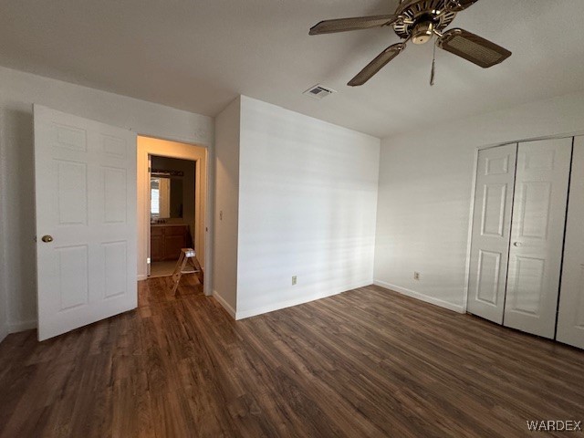 unfurnished bedroom with dark wood-style flooring, a closet, visible vents, and baseboards