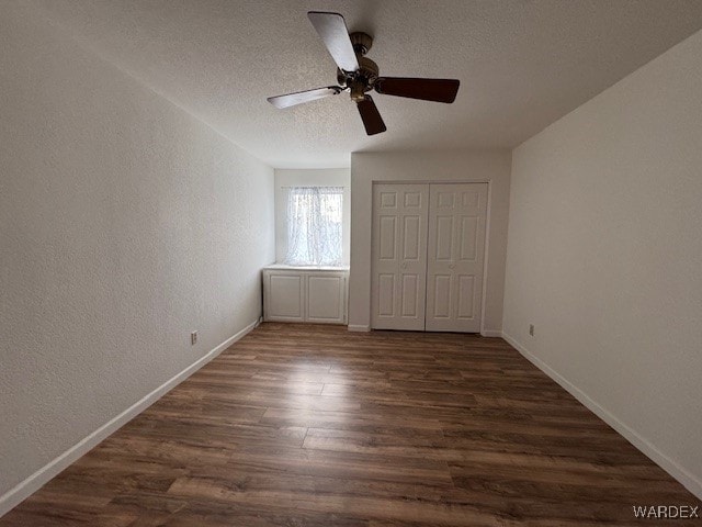 unfurnished bedroom with a textured ceiling, a textured wall, dark wood-type flooring, and baseboards