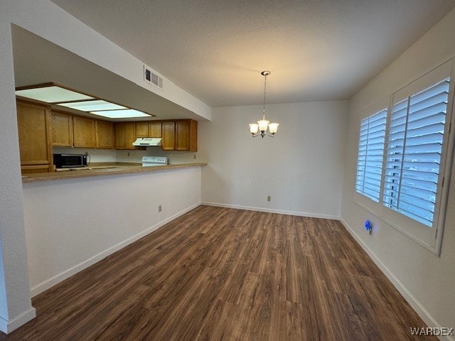 kitchen featuring a chandelier, under cabinet range hood, a peninsula, visible vents, and light countertops