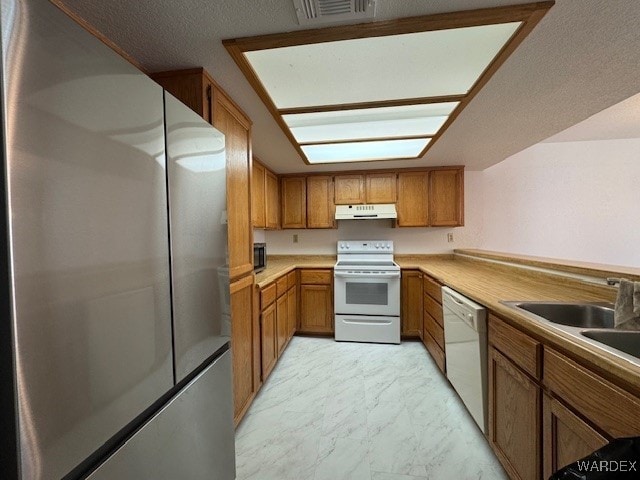 kitchen with under cabinet range hood, white appliances, marble finish floor, light countertops, and brown cabinetry