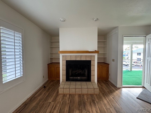 unfurnished living room featuring built in shelves, dark wood-style flooring, a fireplace, and baseboards