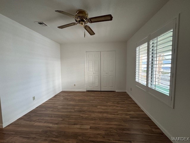 unfurnished bedroom with ceiling fan, dark wood-style flooring, visible vents, baseboards, and a closet