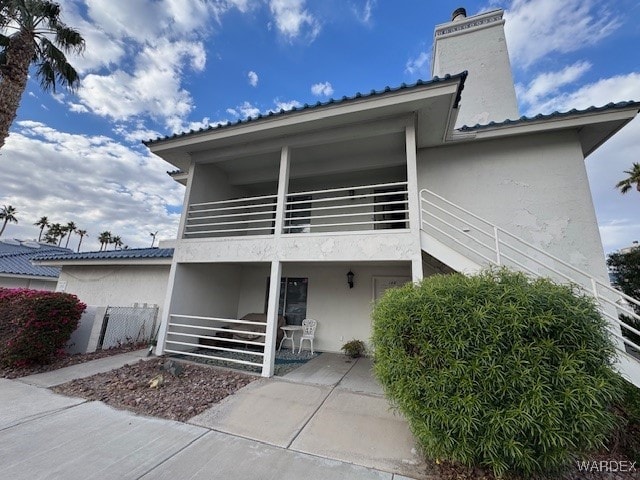 view of front of home with a balcony, fence, stairway, stucco siding, and a chimney