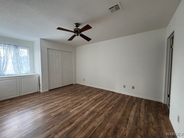 unfurnished bedroom featuring ceiling fan, a textured ceiling, visible vents, baseboards, and dark wood-style floors