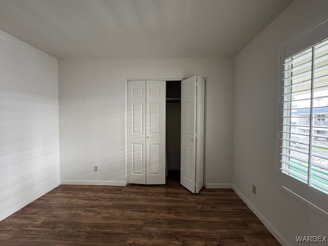 unfurnished bedroom with a closet, baseboards, and dark wood-type flooring