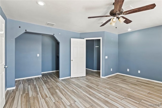 unfurnished bedroom with arched walkways, wood finish floors, a ceiling fan, visible vents, and baseboards