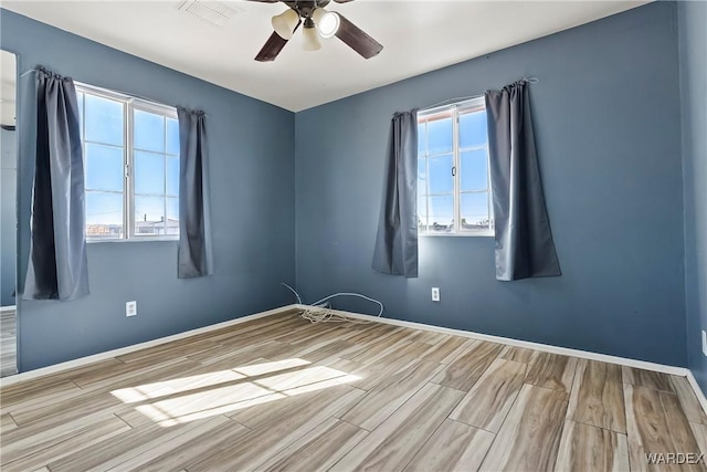 spare room with a healthy amount of sunlight, ceiling fan, baseboards, and wood finished floors