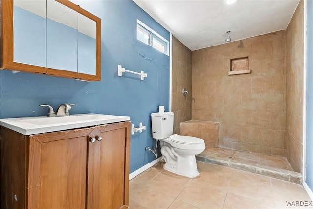 bathroom with toilet, vanity, baseboards, a tile shower, and tile patterned floors