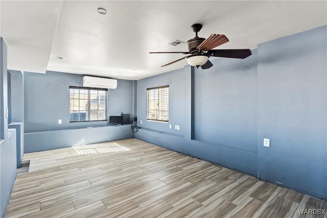 empty room with visible vents, wood finish floors, a ceiling fan, and a wall mounted air conditioner