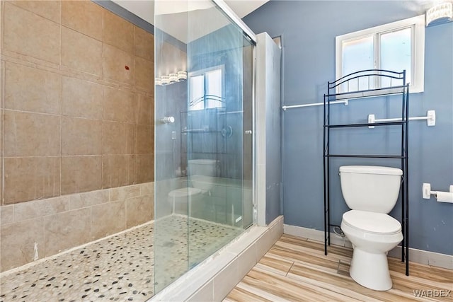 bathroom featuring toilet, a stall shower, baseboards, and wood finish floors