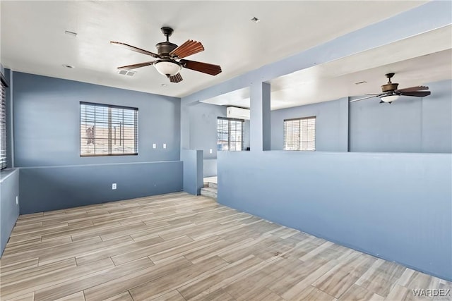 spare room with ceiling fan, visible vents, wood finished floors, and a wall mounted air conditioner