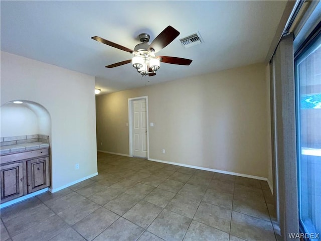 tiled spare room featuring baseboards, visible vents, and a ceiling fan