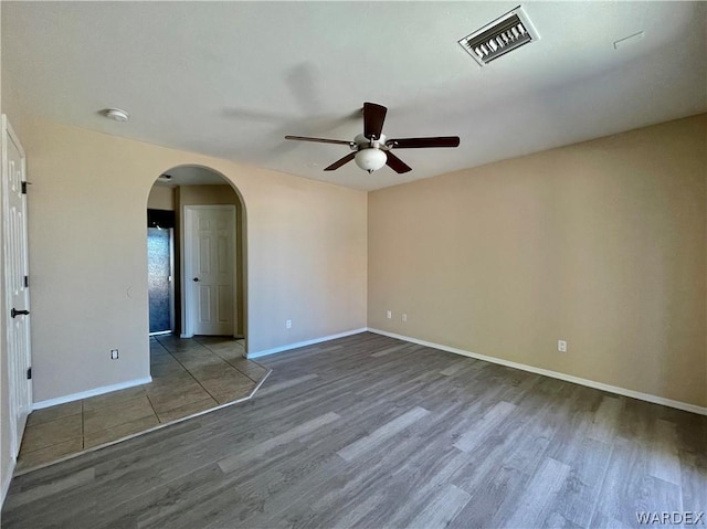 empty room with baseboards, visible vents, arched walkways, ceiling fan, and wood finished floors