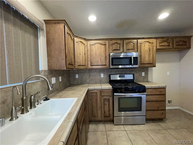 kitchen with tile countertops, appliances with stainless steel finishes, a sink, and brown cabinets