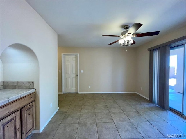 empty room with baseboards, a ceiling fan, and light tile patterned flooring